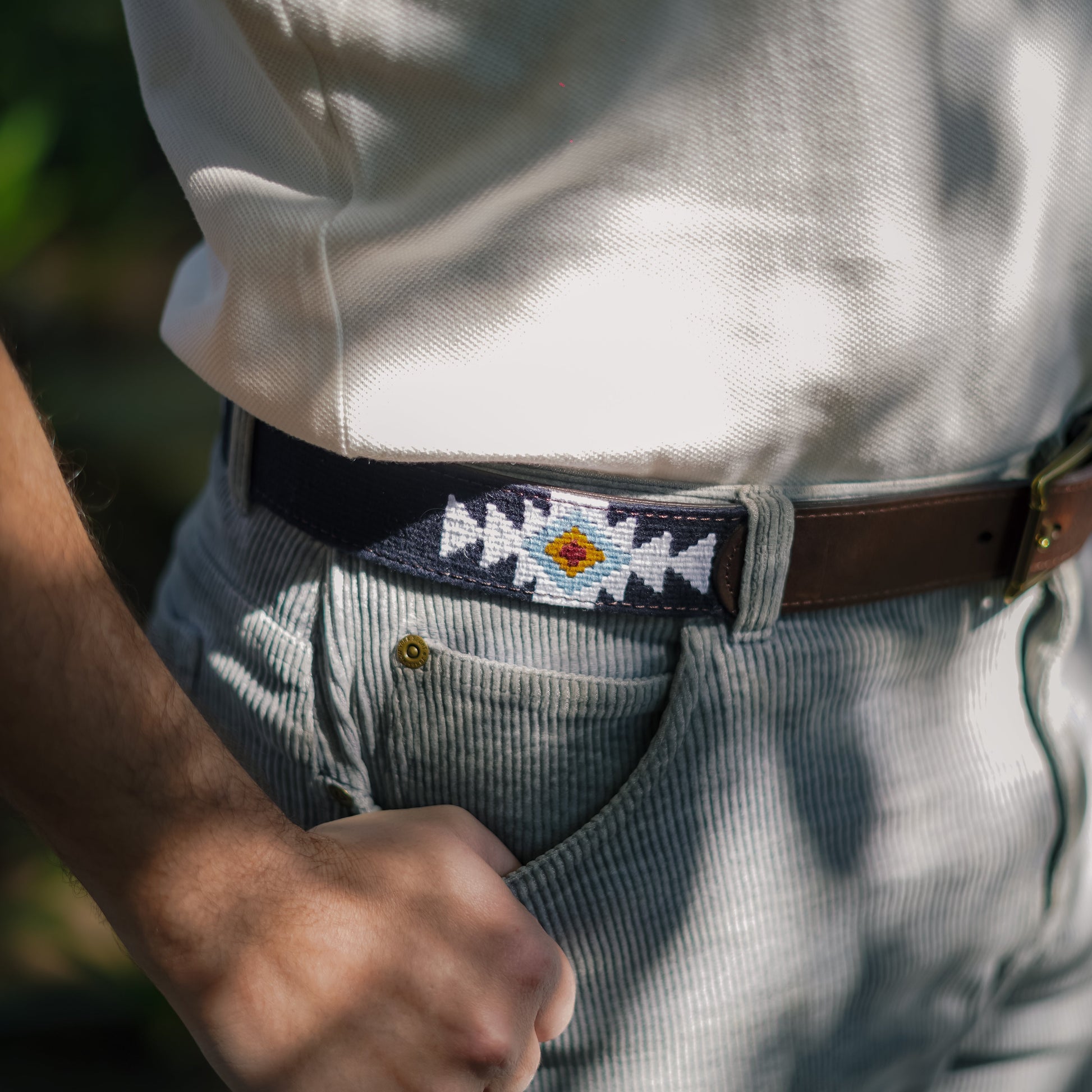 Agua handwoven Maya belt worn with light grey corduroy pants and white polo — navy with white and gold geometric diamond pattern