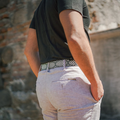 Tikal handwoven Maya belt worn with white chinos and dark t-shirt — forest green and cream geometric pattern against a stone wall in Guatemala