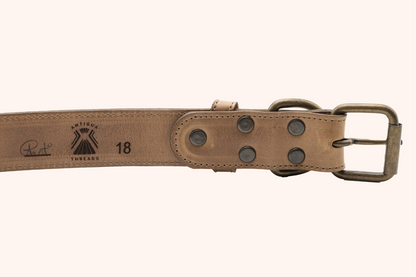 Close-up of a tan leather dog collar, showing the Antigua Threads logo, a signature, and the collar size marked as “18,” featuring sturdy antique brass hardware and rivets.