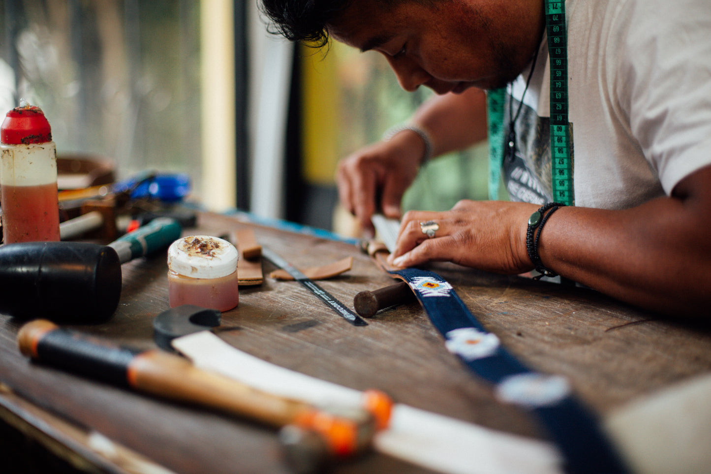 Guatemalan artisan carefully handcrafting a blue woven belt with geometric patterns, using traditional tools in a workshop at Antigua Threads