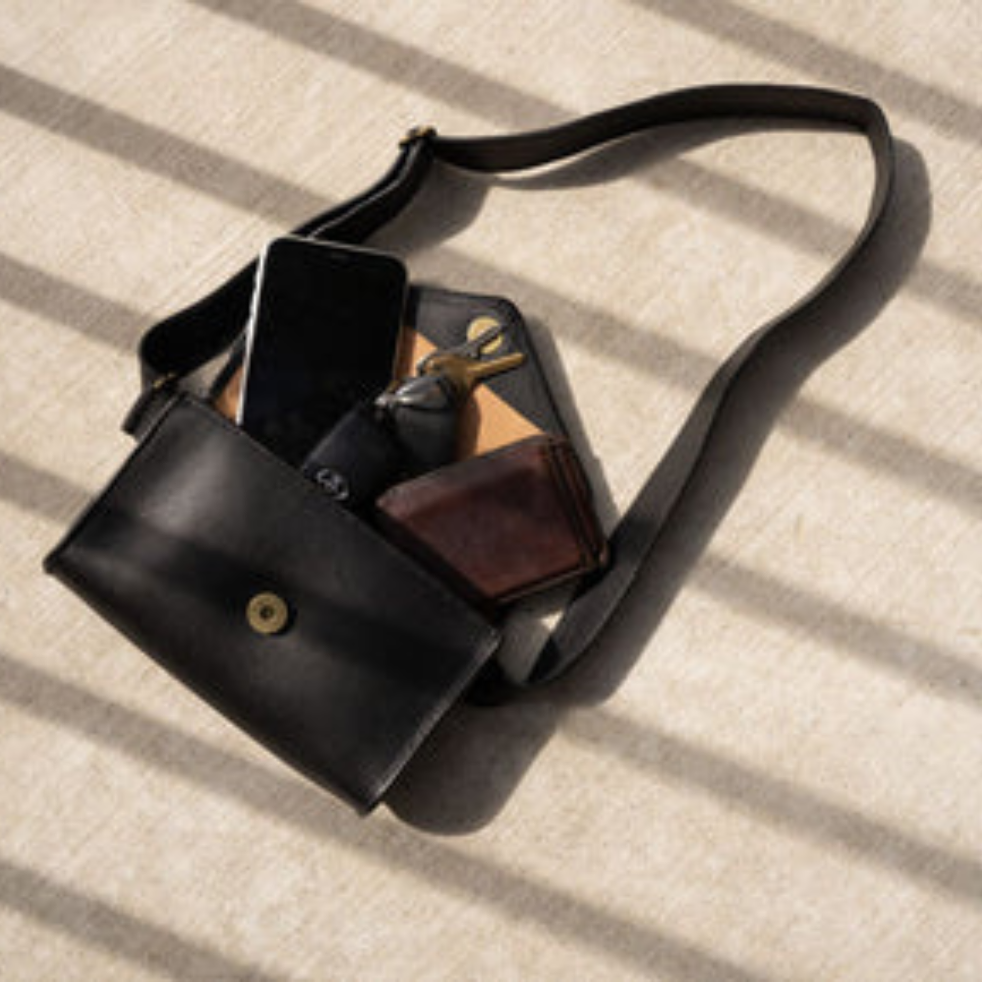 Antigua Threads Everywhere Crossbody Bag in black full-grain leather — open showing phone, wallet, keys, and sunglasses fitting inside