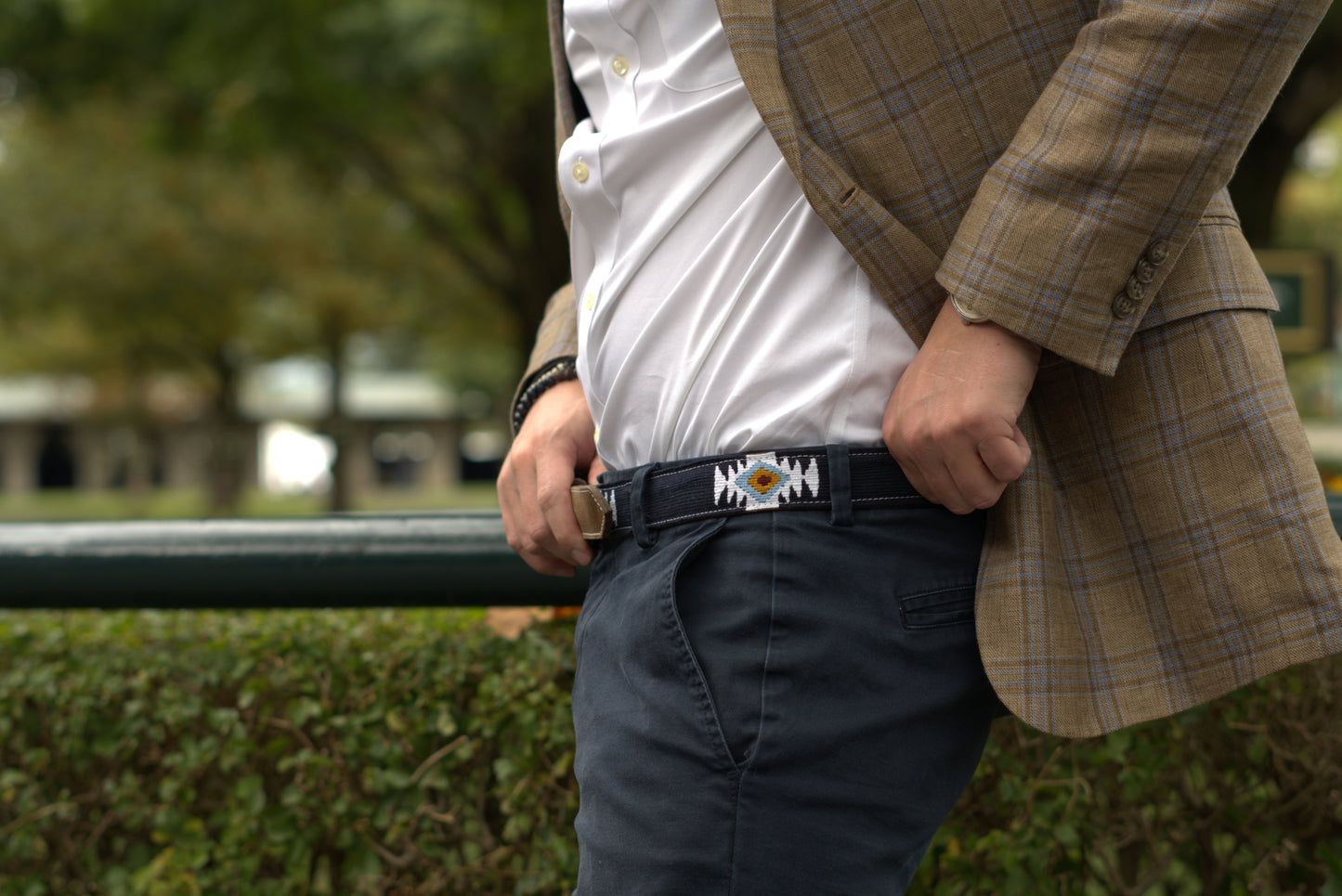 Person wearing a tan plaid blazer and blue pants, showcasing a handwoven blue belt with white, yellow, and turquoise geometric patterns by Antigua Threads