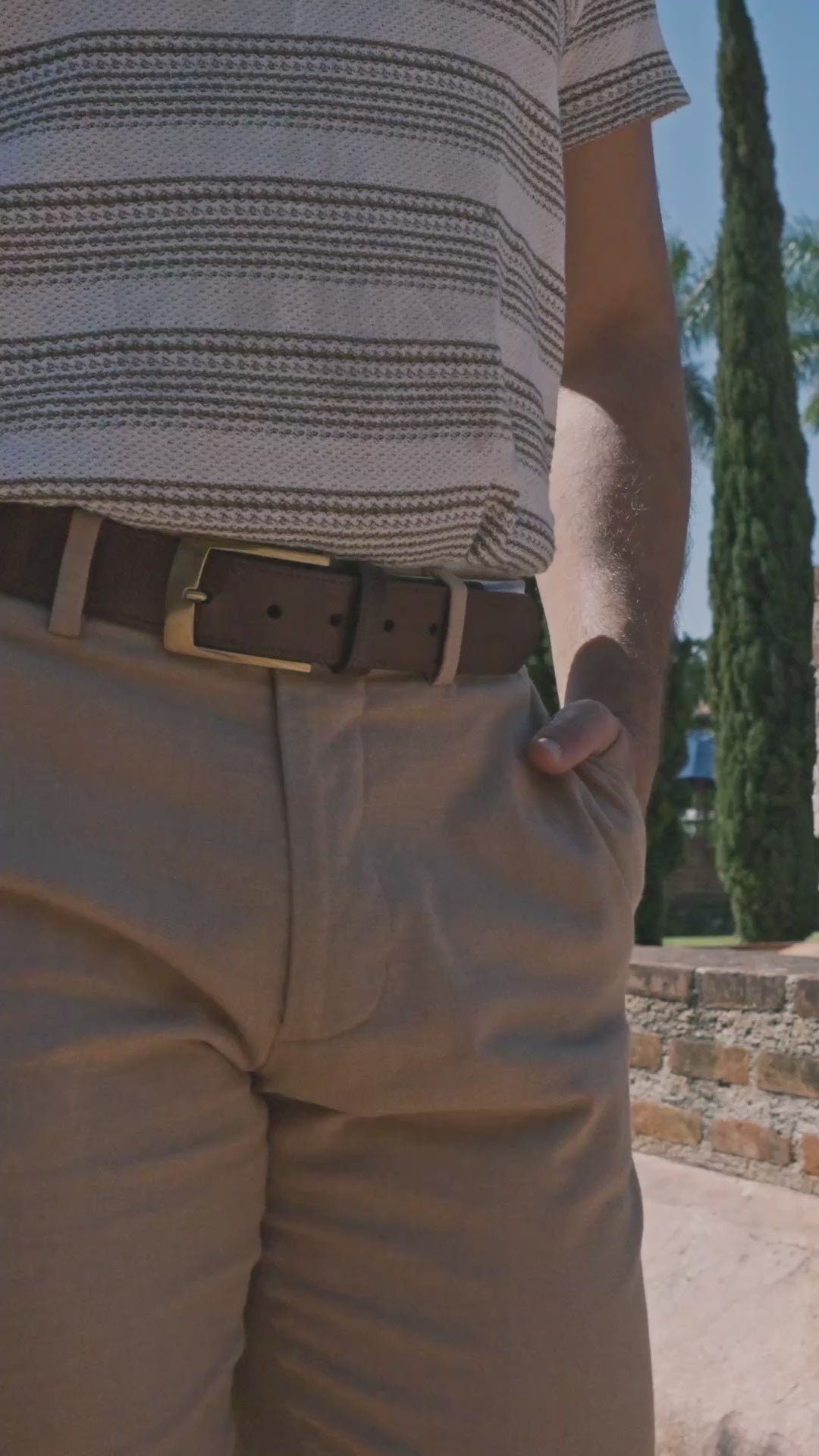 Cobán handwoven Maya belt worn by a model in khaki pants and striped shirt — cream and cobalt blue stripe pattern in an outdoor setting